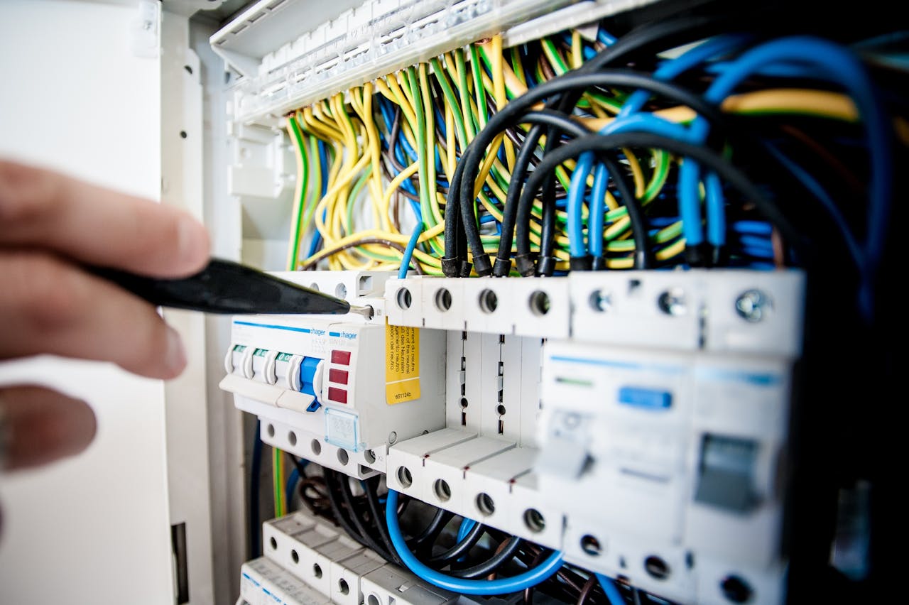 services-02 Hand of electrician working on a circuit breaker panel with colorful wires, ensuring safe electrical connections.